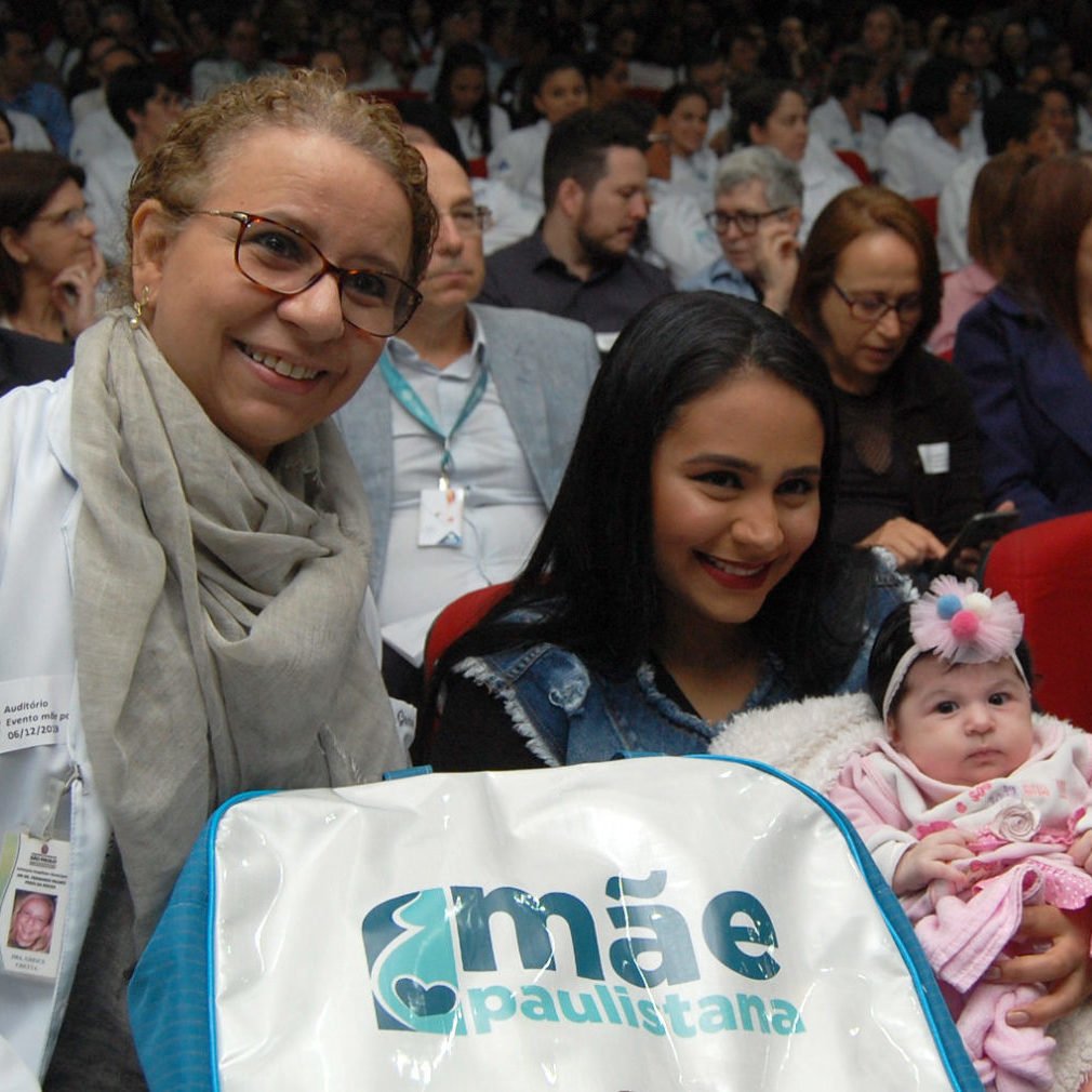 Dra Greice Chetta ao lado de uma moça com o bebê no colo, durante um evento