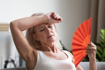 Mulher na menopausa sentindo calor se abana com um leque vermelho